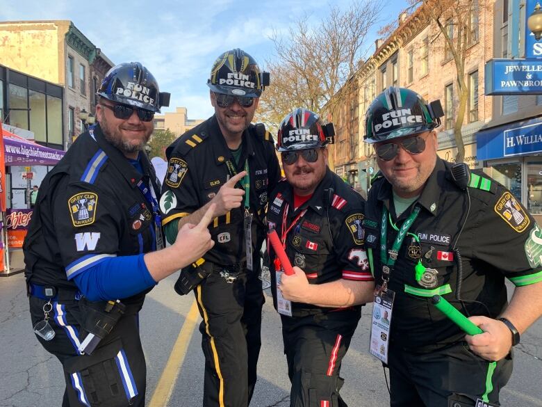 Four people dressed in police costumes group together outside holding up their index fingers. 