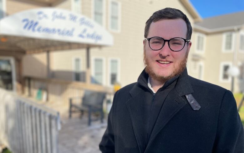 A man with glasses and a beard smiles outside of the nursing home in P.E.I. He wears a black winter coat and glasses. 