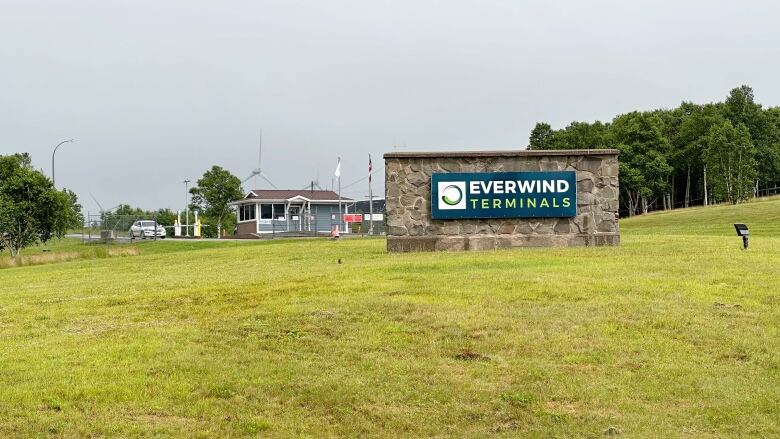 A brick sign on a green lawn says EverWind Terminals, with some buildings and wind turbines in the background.