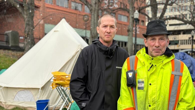 Two men in rain jackets stand in front of a yurt-style tent.