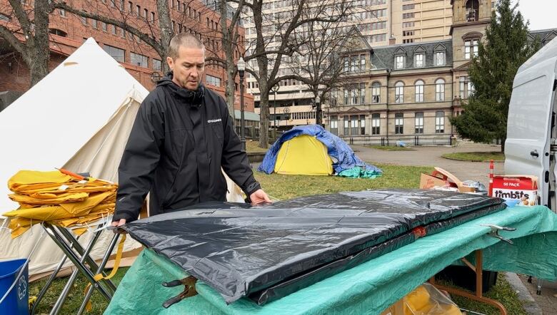 A man covers a mattress pad with a black garbage bag.