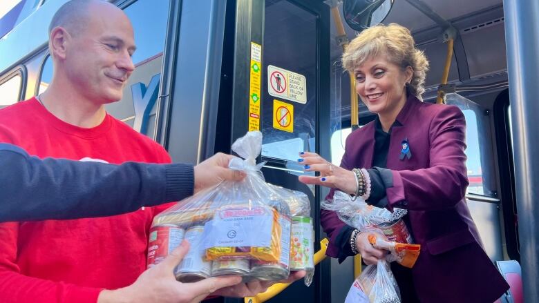 A plastic bag full of food is passed to a woman standing at the open door of a bus.