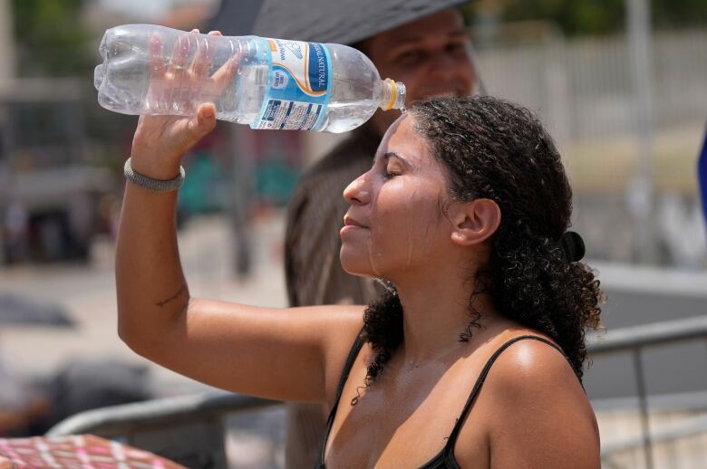 A woman holds up a large bottle of water above her head, pouring it over her face.