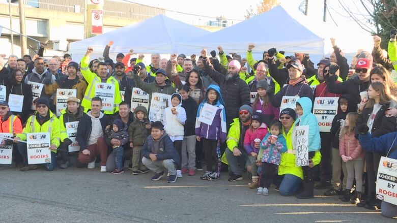 A group of workers with picket signs stand with their hands up. 