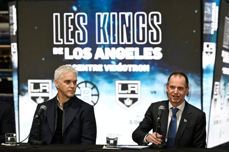 Two men sitting behind a table before a backdrop that says Les Kings de Los Angeles. 