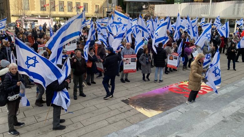 A small group of people wave Israel flags in a downtown plaza.