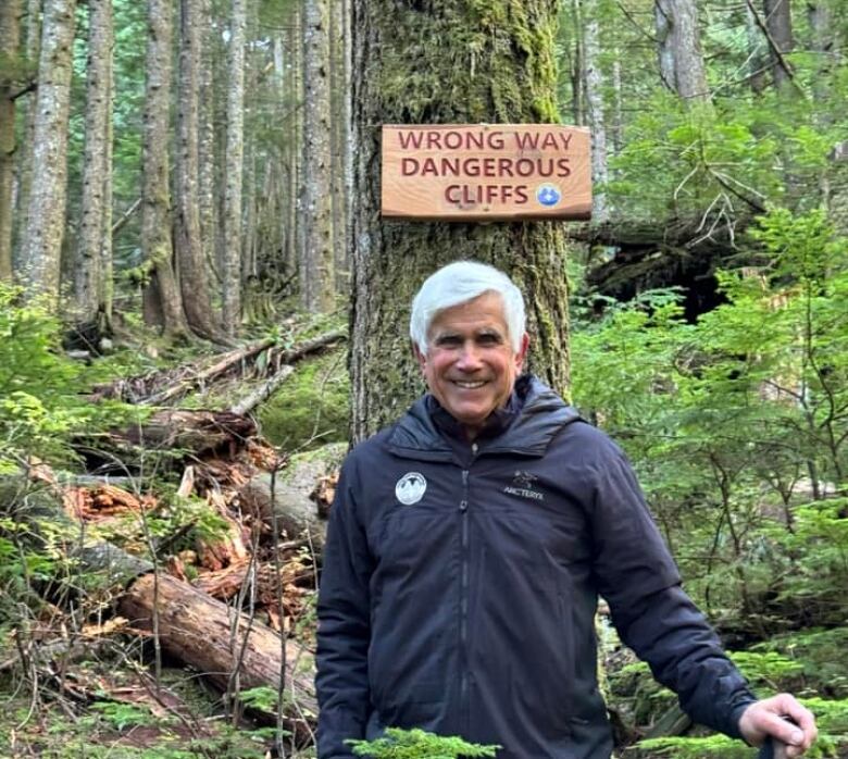 smiling man stands in front of sign reading 