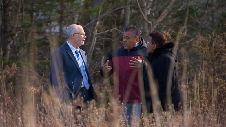 Two men and a woman stand in a field