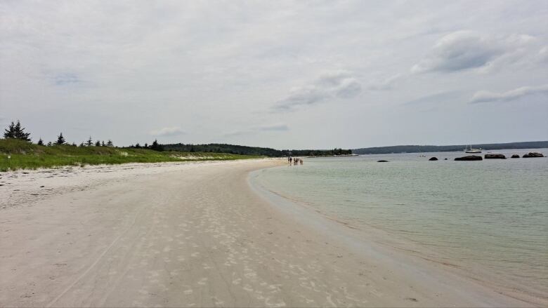 An expansive white sandy beach with clear blue waters under a cloudy sky.