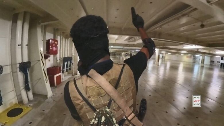 A man holding up a pistol walks on a cargo ship.