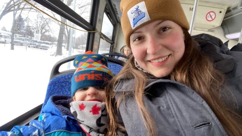 A woman is on the bus with her 4 year-old son, both smiling and bundled up in winter clothing. 