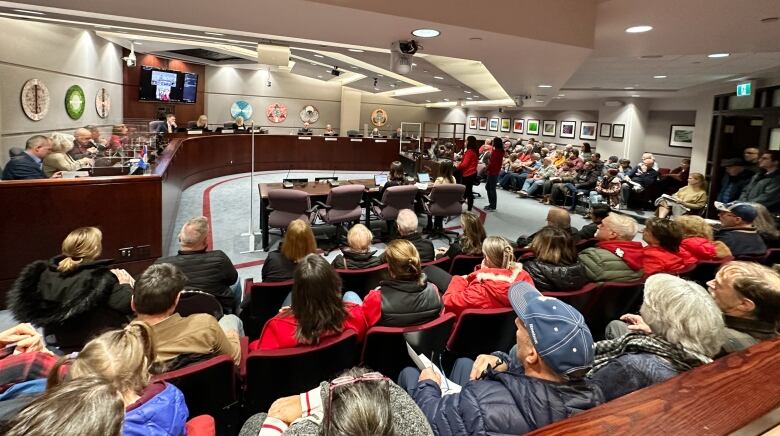 A room with seats around the edges full of people.