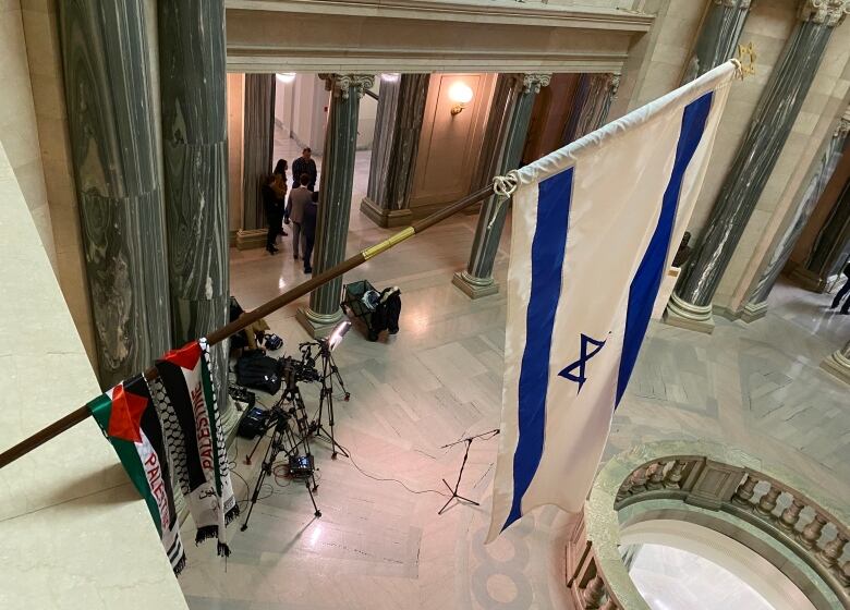 An Israeli flag hangs from a balcony. A banner featuring a Palestine flag is draped lower on the flagpole.