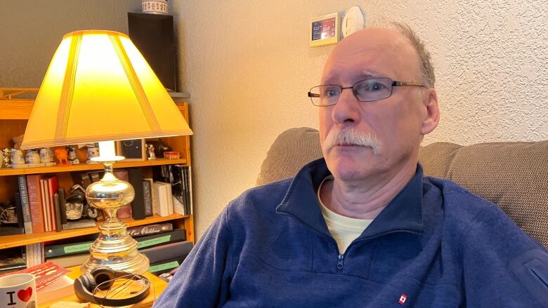 A man in glasses sits on a couch in a home.