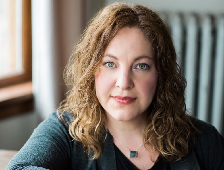 A white woman with curly brown hair and blue eyes looks at the camera. 