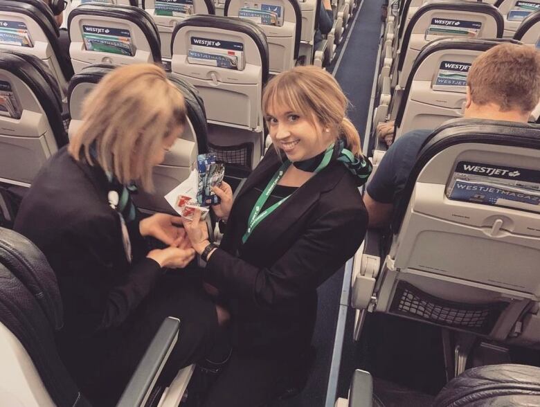 A flight attendant kneels in the aisle of a plane 