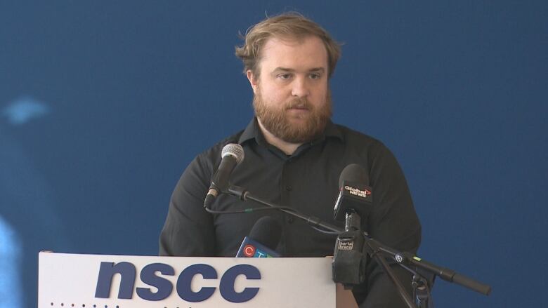 A man with a beard stands at a podium.