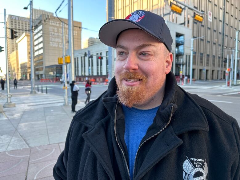 A man in a black jacket stands in a public square.