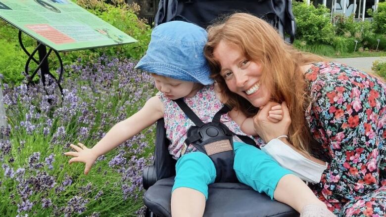 A person snuggles up to a child in a stroller outdoors. 