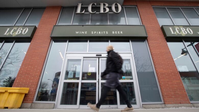 A person walks past the doors of an LCBO store, under a sign saying 'Wine Spirits Beer'.