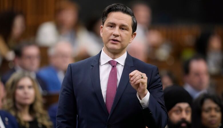 A man dressed in a suit stands and addresses other politicians in the House of Commons.