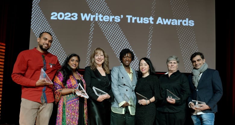 Seven people standing in a row, holding glass awards.