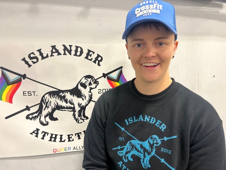 Woman in a baseball cap poses for a picture in a gym. 