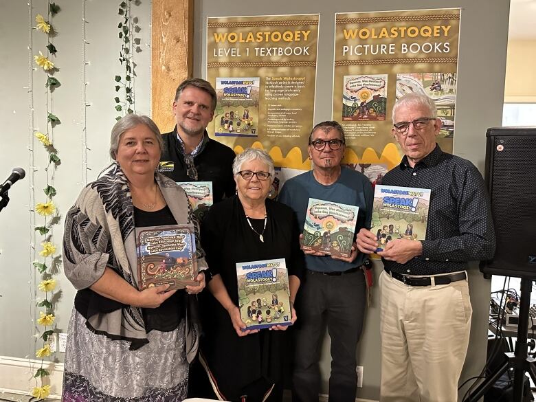 Five people stand together in a group, each one holding a book.