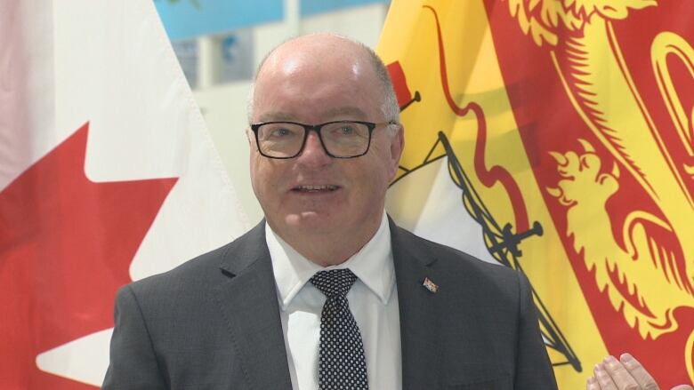 Bruce Fitch speaks in front of the flags of Canada and New Brunswick.