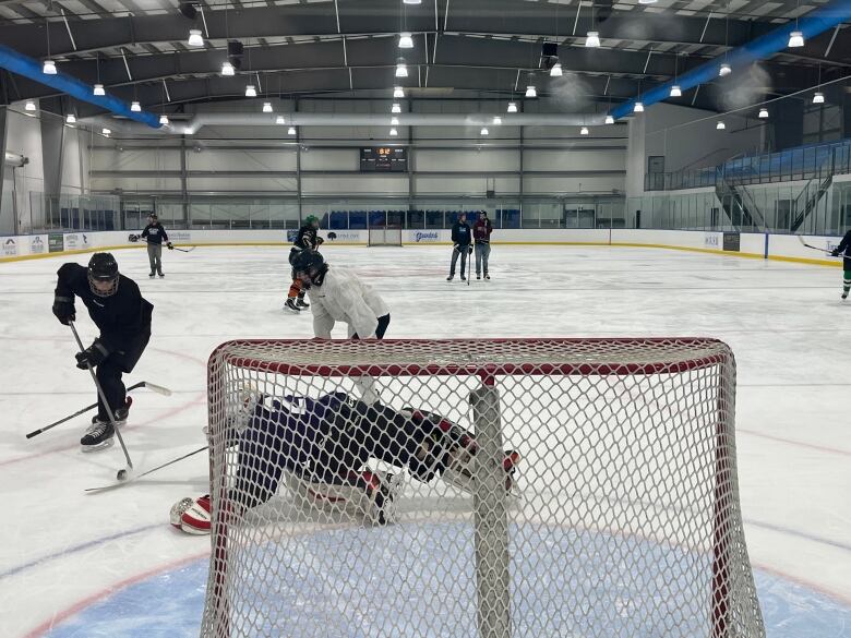 A hockey play makes a shot at the goal in a game of hockey as the goaltender reaches to stop it. 