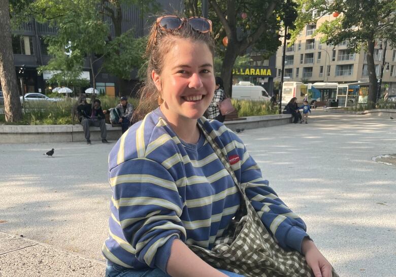 Woman in striped sweater sits outside.