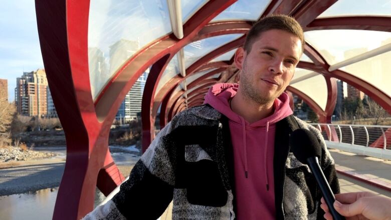 A man stands on a bridge wearing a pink hoodie. 