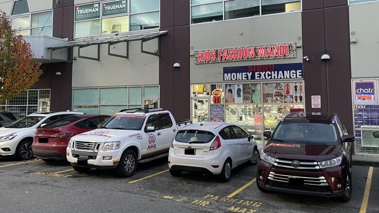 A strip mall with various vehicles, one of which is called Sidhu Money Exchange.