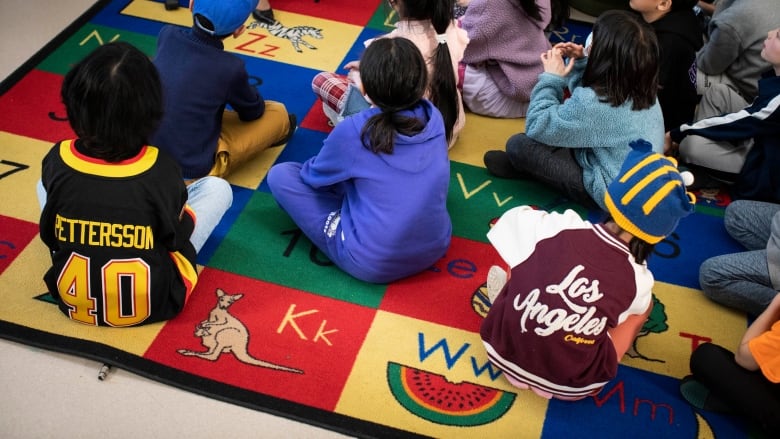 Elementary school students sit on a letter carpet, wearing colourful clothes.