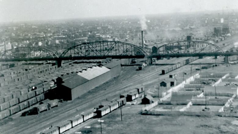 Black and white photo of a steel bridge crossing over a rail yard.