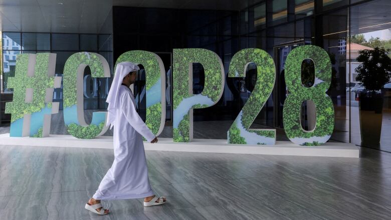 A person in a white robe and white headdress walks past a green 