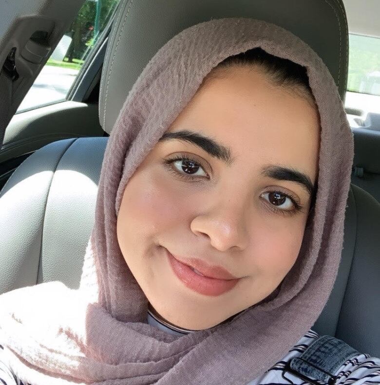 Woman with a light purple headscarf posing for a photo in the front seat of a car. 