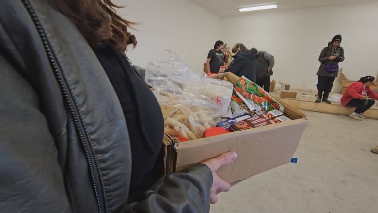 A closeup shows of a small box of groceries being carried by a person.