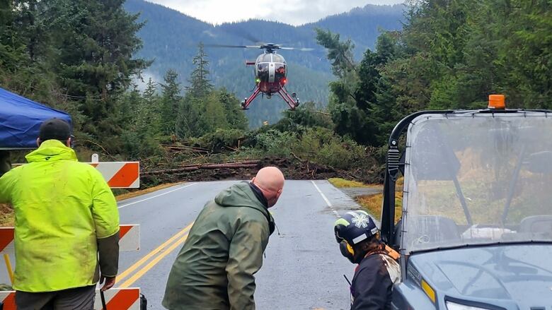 Some people at a roadblock look on as a helicopter prepares to land on the road.