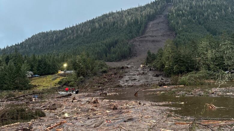 Some debris floats just off shore at the base of a mountain where a landslide area is visible.