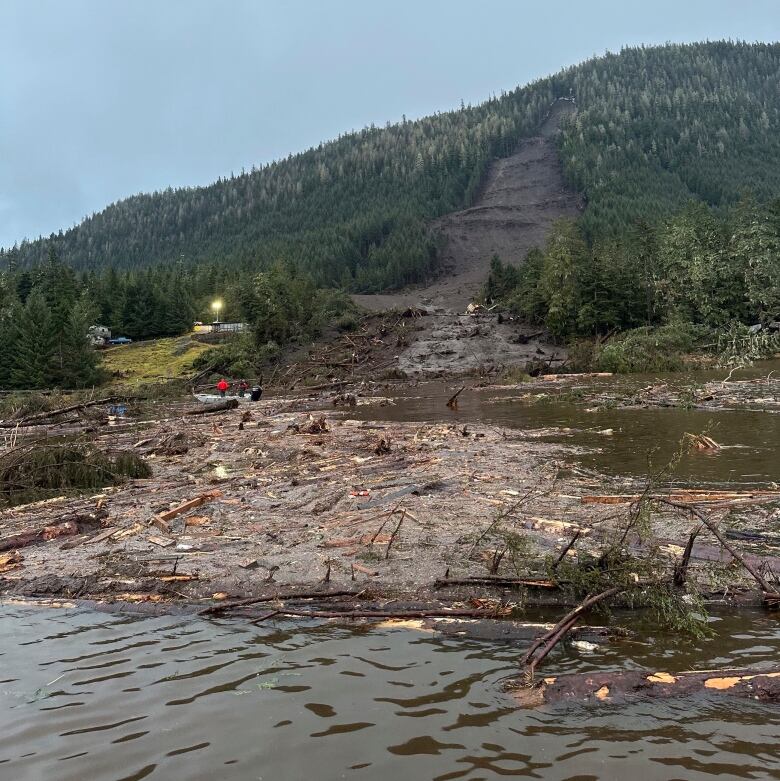 Some debris floats just off shore at the base of a mountain where a landslide area is visible.