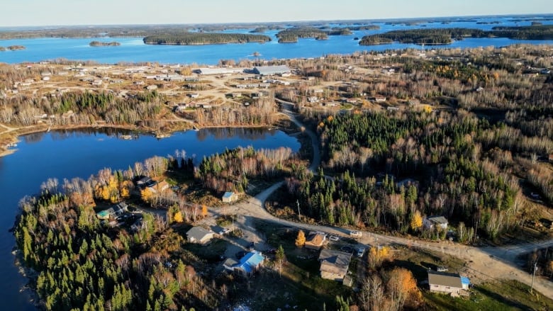 An aerial photo shows a community beside an island-dotted lake in a forested area.