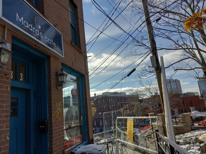 Corner of a building with a cafe sign madras on it, next to a construction site.