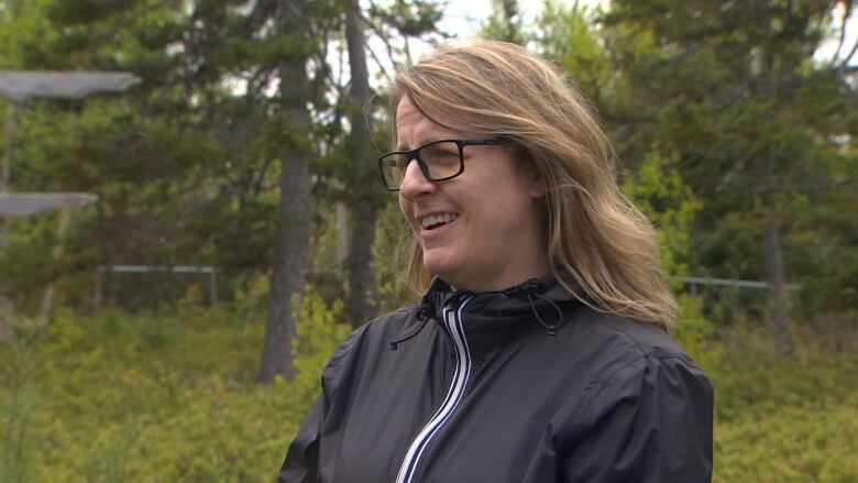 A woman stands outdoors. She is wearing a windbreaker. 