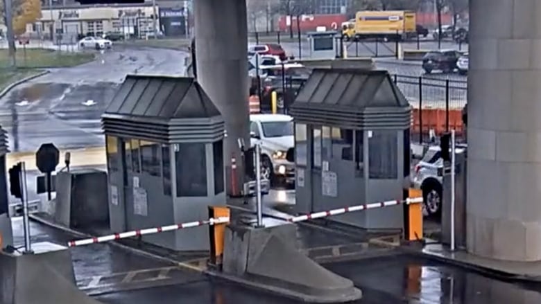 Security camera footage shows vehicles at a toll booth, In the background, a vehicle travels toward a toll booth. 