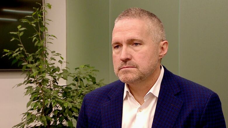 A businessman sits in a boardroom with a plant in the background.