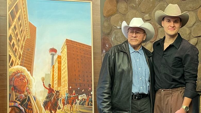 Two men in cowboy hats stand next to two framed posters.