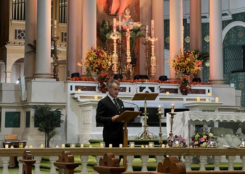 A man is delivering a speech at a podium in front an elaborate and ornate Catholic structure.