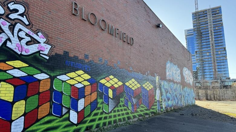 An exterior brick wall of the former Bloomfield School in Halifax, N.S., with graffiti painted over the lower half. A high-rise building and crane are seen in the background.