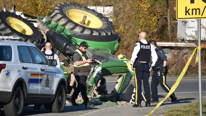 Police officers are seen around a green tractor on its side. 